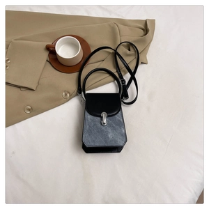 Detail of grey-blue denim texture and black leather flap with silver clasp on handbag