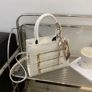 White faux leather tote bag with decorative gold zippers and silk scarf handle detail