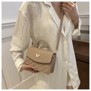 Detailed view of beige crossbody bag featuring diamond quilting and a white butterfly clasp