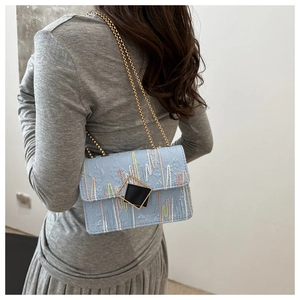 Detail of light blue embroidered chain bag with colorful stitching and gold hardware