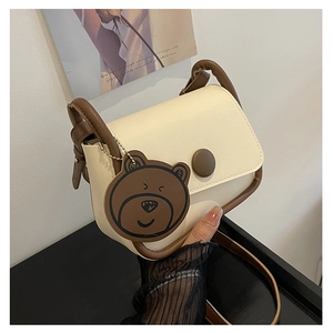 Détail du sac bandoulière crème avec bordure marron et breloque ours mignonne