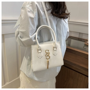 Detail of white box bag featuring golden SS logo with refined metal tassels and handle