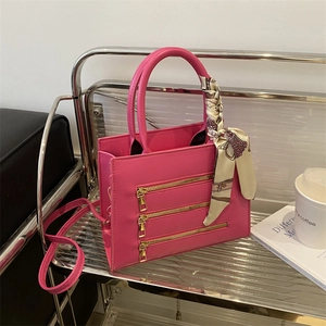 Detail of fuchsia square bag with gold zippers and decorative silk scarf on handle