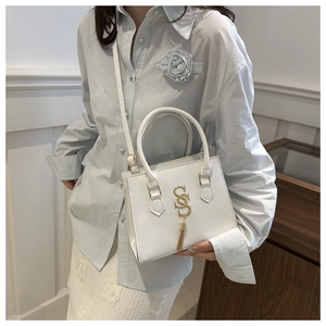 Detailed close-up of white leather handbag with gold metal logo and fringe tassel detail