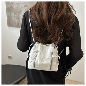Detail view of white drawstring bucket backpack with silver chain strap and bow zipper