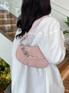 Pink pleated shoulder bag with heart charms and pearl chain shown on model in street style
