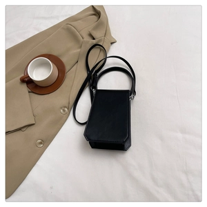 Detail of minimalist black matte leather square handbag on white fabric with long strap