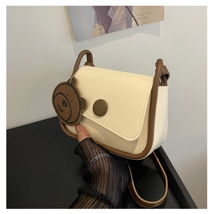 Détail du sac besace crème avec bordure marron et breloque ours mignon en situation réelle