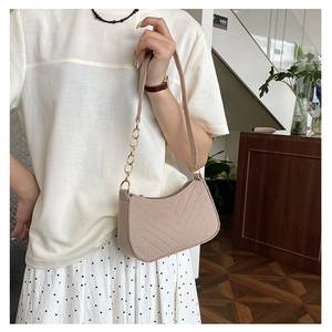 Detail of beige underarm bag showing V-shaped quilting and gold chain strap on model