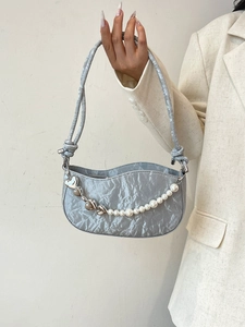 Silver pleated shoulder bag with pearl and heart chain detail shown in hand
