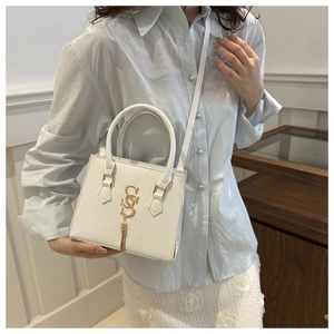 Close-up of white crossbody bag featuring golden double S logo and metallic tassel details