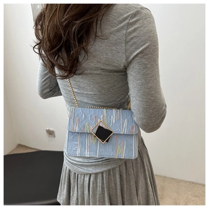 Detail of light blue crossbody bag with wave stitching and gold chain on model