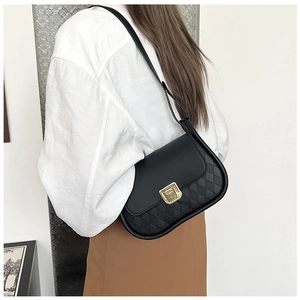 Detail of black quilted shoulder bag featuring gold square lock and leather strap on model
