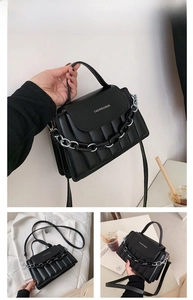 Detail of black quilted crossbody bag with top handle and decorative chunky chain strap