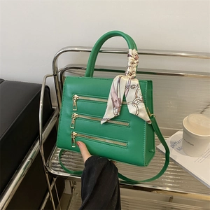 Detail of green leather handbag featuring decorative triple zippers and silk scarf handle