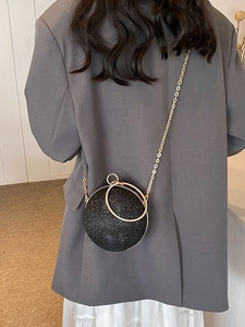 Sparkling black spherical clutch bag with gold chain strap shown on a model
