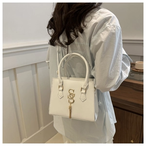 Detail of white PU leather handbag with gold SS pendant on female model shoulder