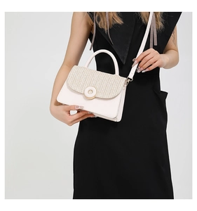 Detail of minimalist cream handbag with woven straw texture flap and round metal clasp