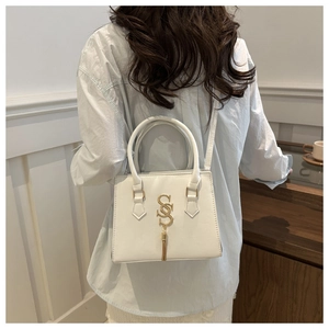 Close-up of white crossbody bag with gold S pendant and tassel in a cozy indoor setting