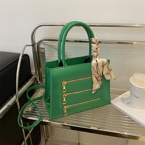 Detail of green square bag featuring gold zippers and handle wrapped in floral silk scarf
