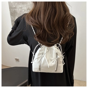 Detail of white leather drawstring backpack featuring ribbon bows and chain straps