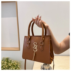 Detail of caramel faux leather handbag featuring a gold S-pendant and metal fringe
