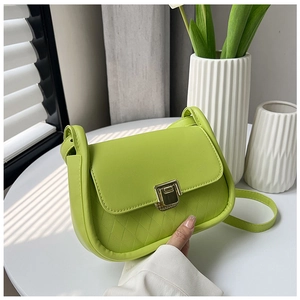 Detail of neon green crossbody bag with quilted texture and gold lock on a white table