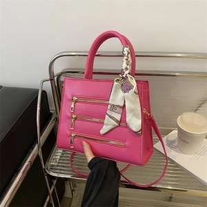Close-up of fuchsia leather handbag with triple gold zippers and decorative scarf