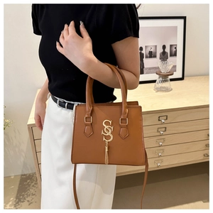Detailed view of the gold SS logo and fringe on the brown leather crossbody square bag