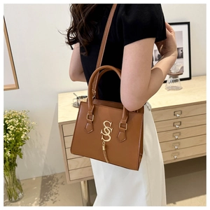 Detail of caramel brown handbag with golden S-logo pendant and tassel on the side