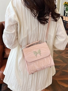 Pink pleated crossbody bag with silver butterfly accent shown on a model in white top