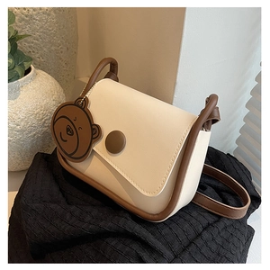 Détail du sac besace beige avec bordures marron et charmant porte-clés ours en cuir