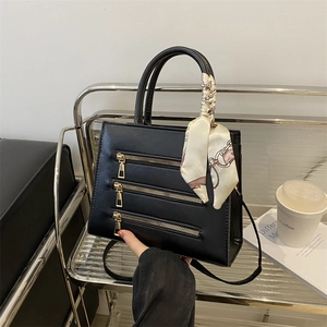 Detailed view of black handbag with triple metal zippers and elegant printed silk scarf handle