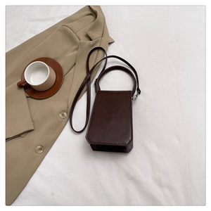 Detailed close-up of dark brown trapezoid leather handbag on neutral background