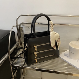 Detail of black crossbody bag featuring gold zipper accents and a stylish silk scarf wrap