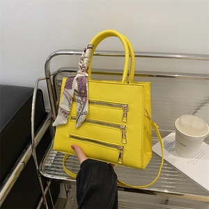 Close-up of bright yellow handbag featuring triple decorative zippers and floral silk scarf