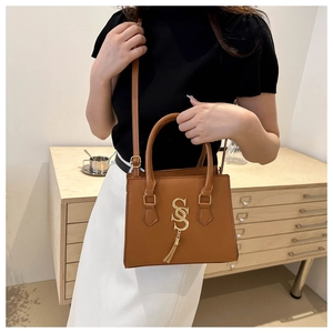 Close-up of structured brown handbag with gold interlocking S logo and tassel detail
