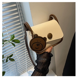 Détail du sac selle minimaliste en cuir crème avec bordures marron et petit pendentif