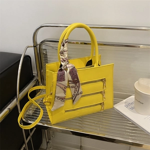 Detail of bright yellow tote bag featuring triple zipper design and floral silk scarf charm