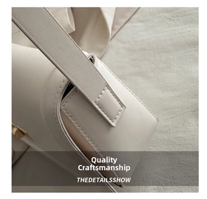 Detail view of cream leather shoulder bag with precise white stitching and gold hardware buckle