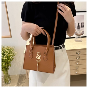 Detail of caramel leather handbag featuring gold S-shaped logo and elegant metal fringe