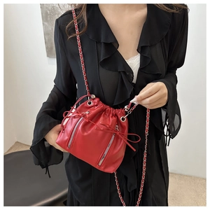 Detail of red drawstring bucket bag with silver zippers and metal chain strap