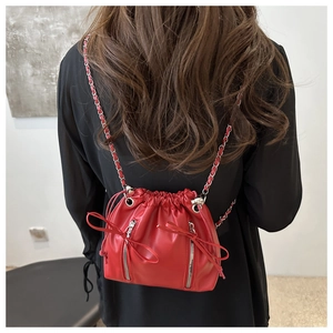 Detail of red drawstring bucket bag with decorative zippers and metal chain strap