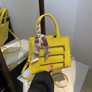 Detail of yellow handbag featuring triple zip design and a patterned silk scarf handle