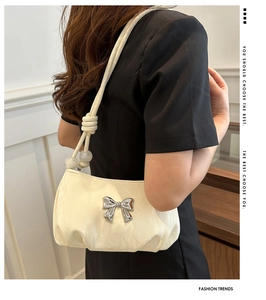 Detail of a pleated cream underarm bag featuring a silver bow and beaded strap