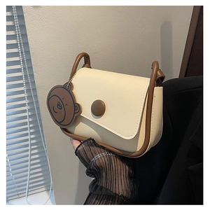 Détail du sac de selle crème et marron avec breloque ours et boucle décorative ronde