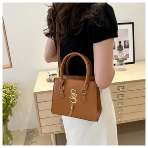 Brown leather handbag with gold S-logo shown on model for size and style reference
