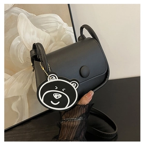 Détail du sac de selle noir en similicuir avec boucle magnétique et breloque ourson