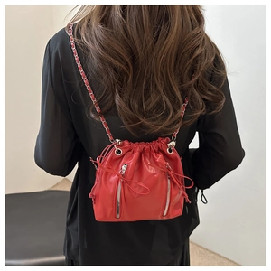 Detail of red drawstring bucket bag with dual zippers and metal chain strap on model