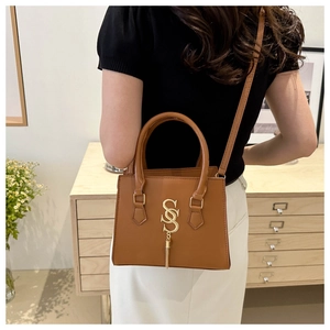 Detail of caramel leather square handbag with golden SS logo and metallic fringe tassel